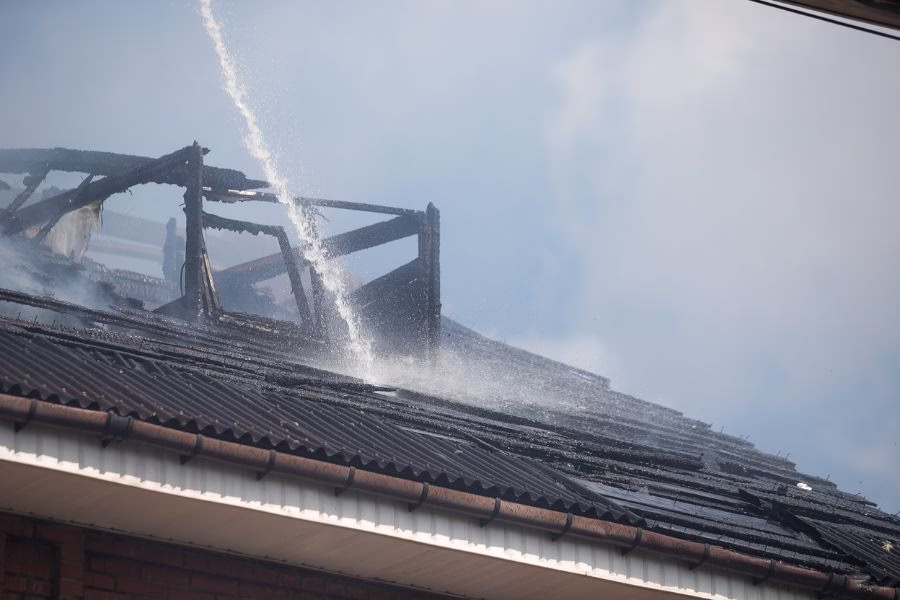 Water being sprayed on the roof of a house that was burnt in a fire.